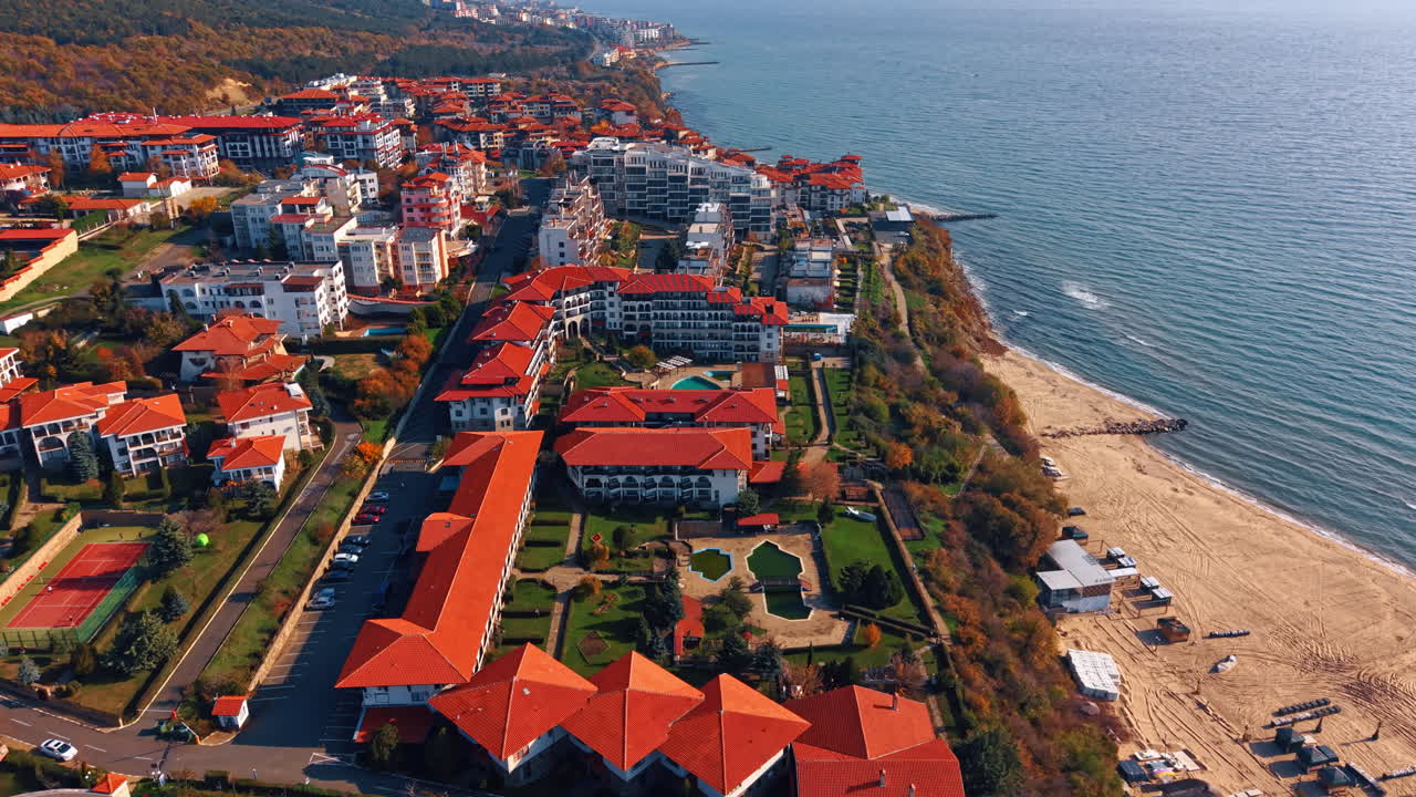 Belos hotéis com telhados vermelhos nas encostas verdes das rochas. Voo ao longo da ensolarada praia de areia do Mar Negro em Nessebar, Bulgária