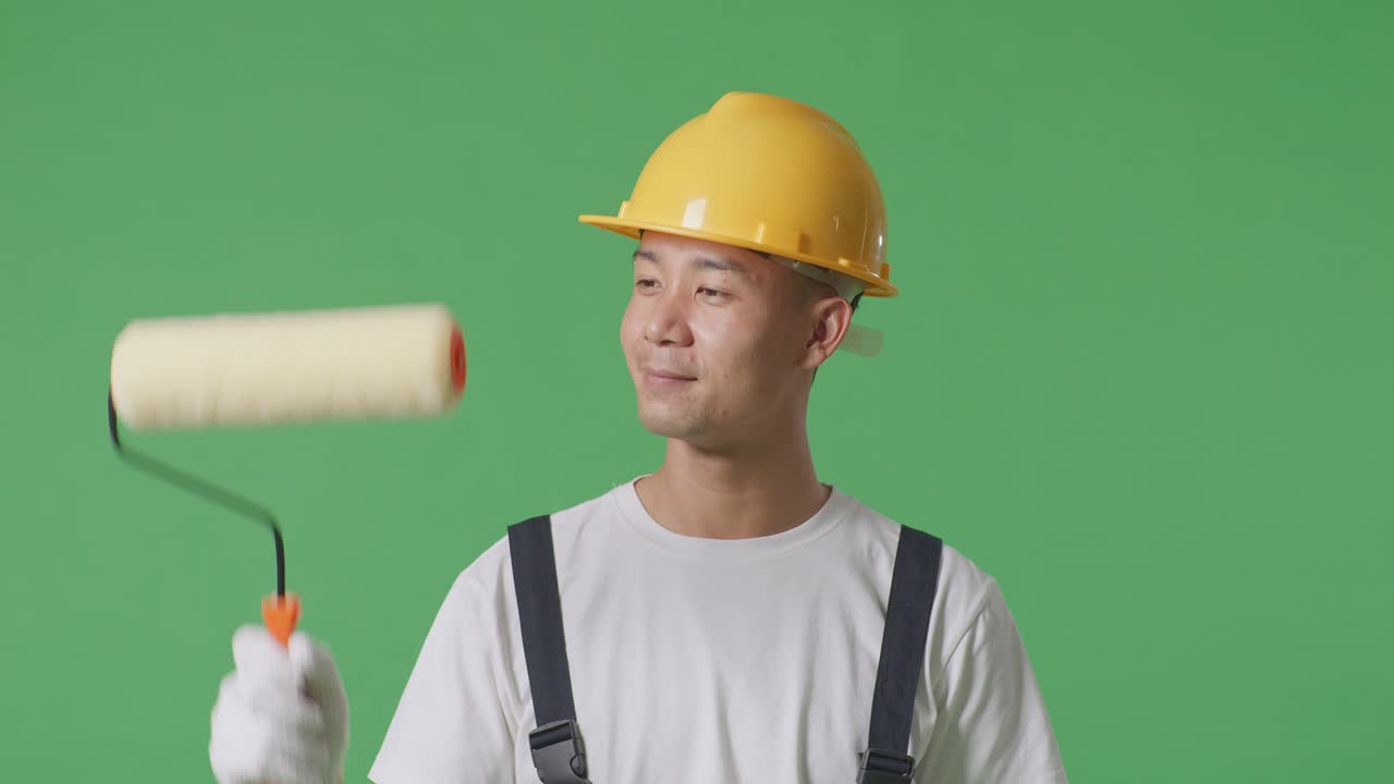 Close Up Of Asian Man Painter Wearing Safety Helmet Painting And Smiling In The Green Screen Background Studio