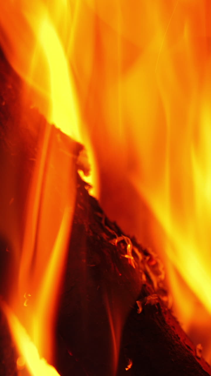 Vivid flame on wooden logs. Orange and yellow fire burning in fireplace. Bright motion of fire tongues. Macro shot. Vertical video