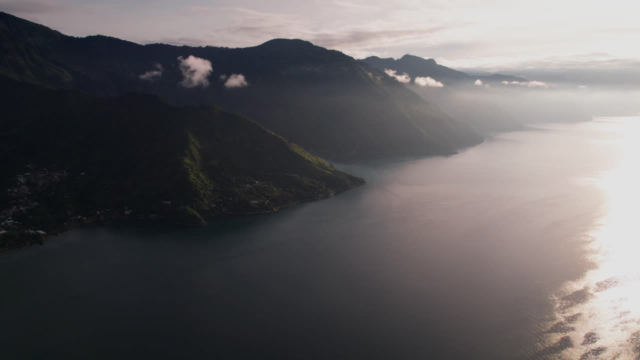 A breathtaking high-altitude drone shot captures a long pier extending into the glassy, reflective waters of Lake Atitlán at sunrise