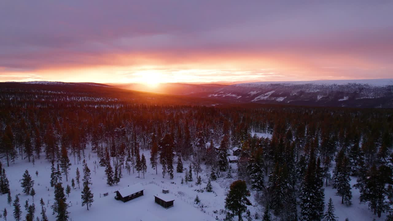 Hytter og vinterlig skoglandskap i en brennende solnedgang