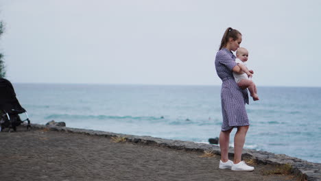 with the sea and beach as a backdrop, a poignant portrait reveals a mother's affectionate kiss for her daughter. the family enjoys their vacation, and the mom tenderly embraces her toddler