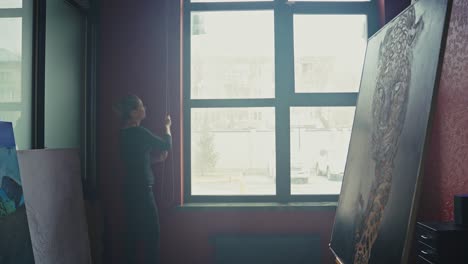 woman adjusting blinds in art studio
