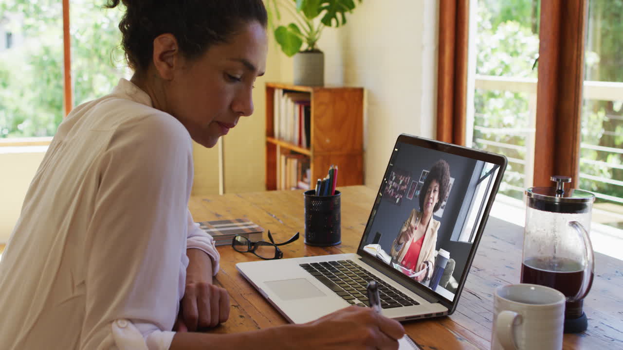 African american woman taking notes while having a video call on laptop at home