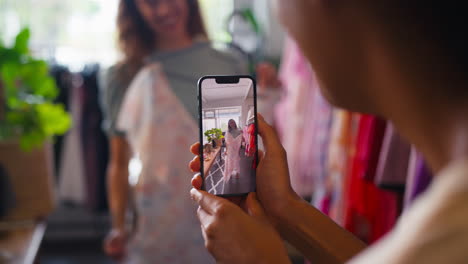 two friends shopping for clothes in fashion store taking video of dress