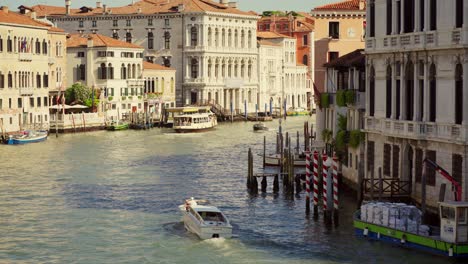 Taxi-boat-on-the-water-of-Canal-Grande-in-Venice,-Italy,-is-cruising-under-a-bridge-in-the-morning-sunlight