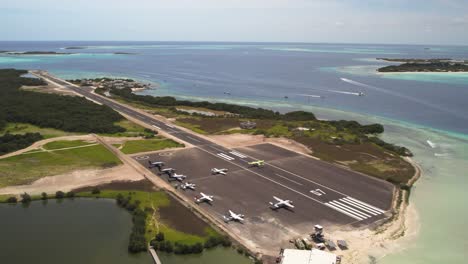 A-small-airport-on-gran-roque-with-planes-and-surrounding-turquoise-waters,-sunny-day,-aerial-view