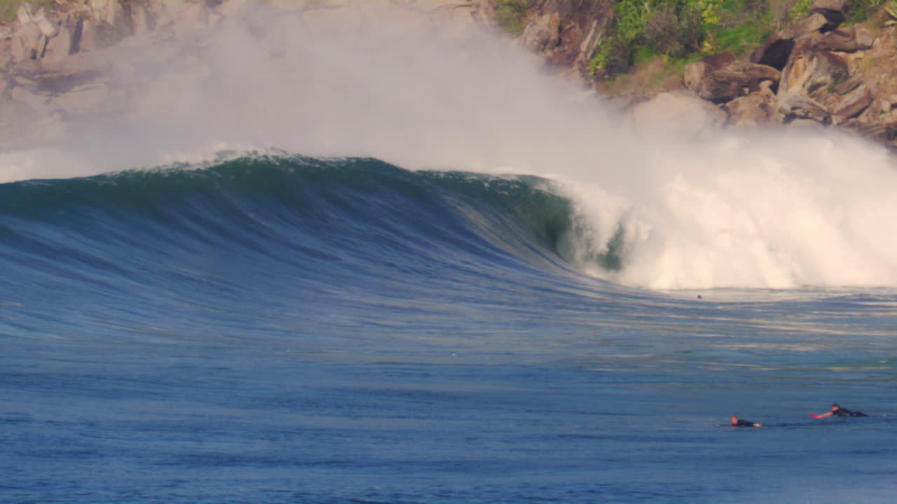 Slow motion view of surfers in lineup as empty wave goes unridden crashing and rolling in stunning vortex of strength