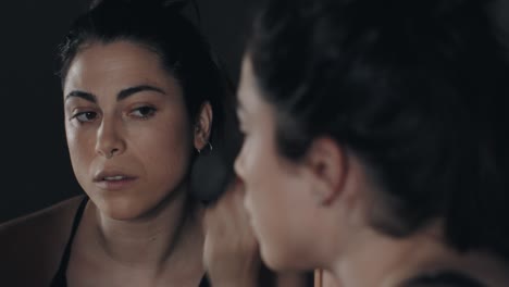 Close-up-of-young-woman-applying-make-up-with-brush-in-front-of-a-mirror