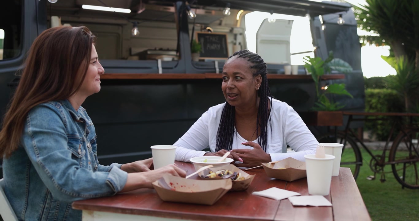 Two Diverse Women Eating and Talking at an Outdoor Food Truck