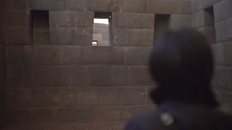 an asian tourist, donning sunglasses, turns around in admiration of the splendid qorikancha temple made of indigenous rocks from the incas in cusco, peru