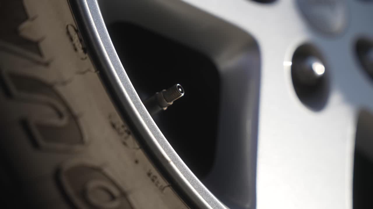 Close-up hand tightening tire valve cap on SUV wheel in sunlight