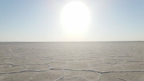 Eine-Intensive-Ewigkeitsdrohnenaufnahme-Aus-Niedrigem-Winkel-über-Den-Salzebenen,-Die-Der-Sonne-Und-Dem-Horizont-Entgegenfliegt