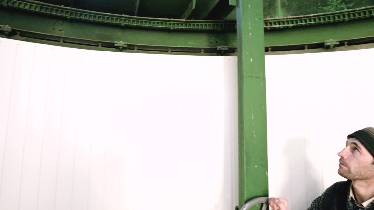 남성 연구원은 코카서스 산맥의 과학 연구 관측 스테이션에서 태양 관측소의  문 열기 메커니즘의 수동 바를 회전시니다.