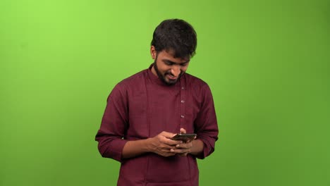 Handsome-man-writing-a-message-on-smartphone-and-looks-towards-camera,-isolated-on-green-screen