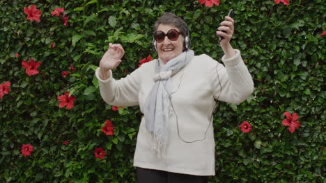 portrait of senior caucasian woman dancing enjoying playful dance arms raised listening to music on headphones wearing sunglasses in outdoors garden background