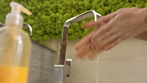 woman washes her hands with liquid soap over the toilet sink