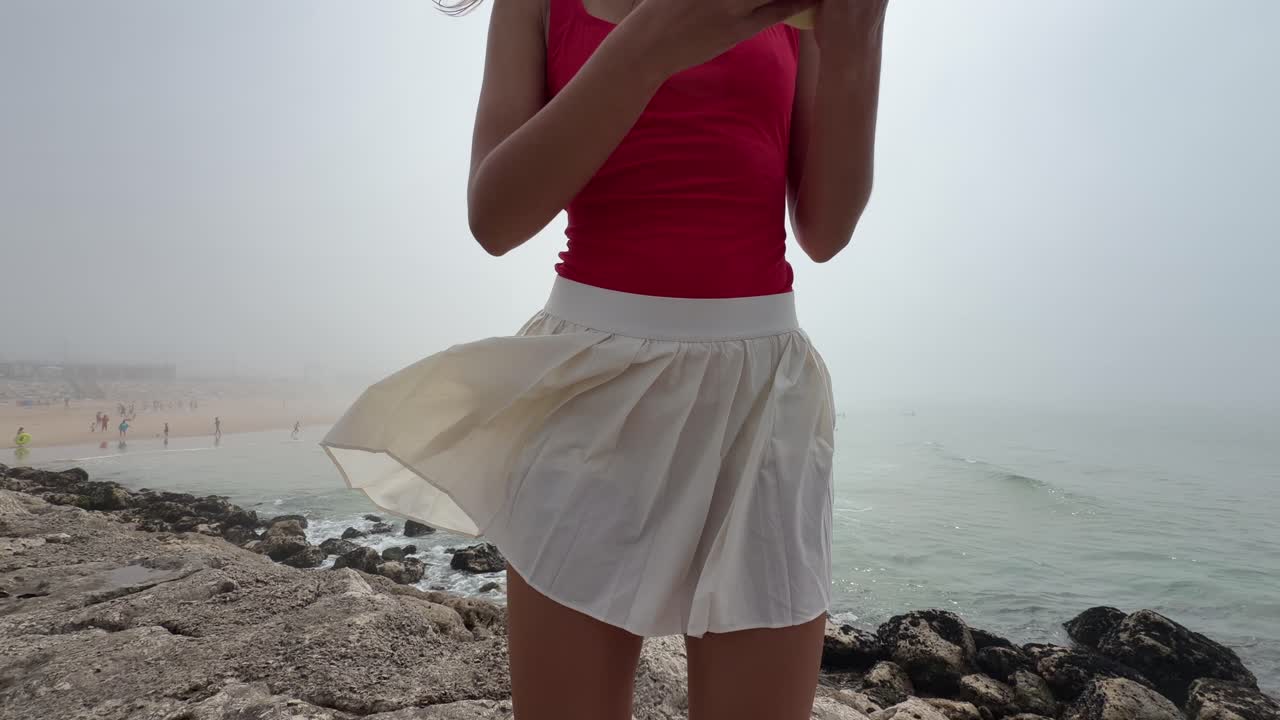 Giovane donna in piedi su un litorale roccioso che guarda il telefono