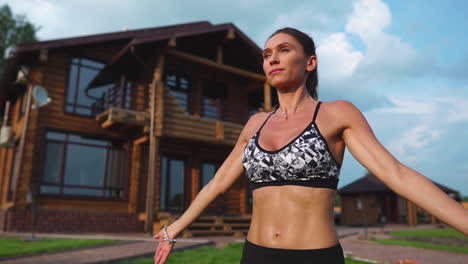 mujer delgada y hermosa en ropa deportiva en el fondo de la casa en el césped realiza saltos para el entrenamiento cardiovascular y la quema de grasa