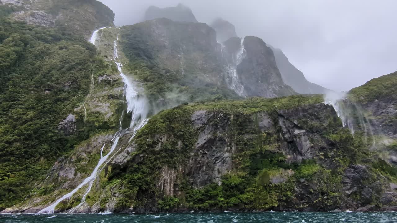 el viento tormentoso interfiere con la cascada que fluye por los escarpados acantilados de milford sound.