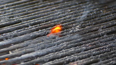 a small flame burns on some old food on a lit grill in slow motion