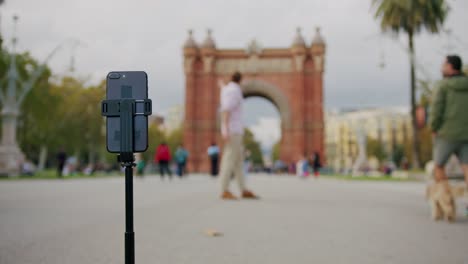 Man blogger making videos using selfie stick phone smartphone taking photo with dance for internet blog on street. Young guy tourist having video call on cellphone walking outdoors in Barcelona spain