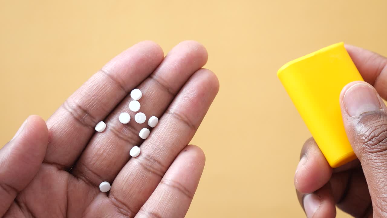primer plano de una mano sosteniendo pastillas blancas y un recipiente amarillo