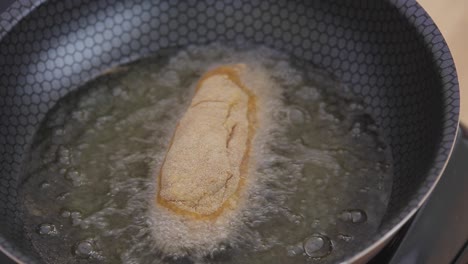 oil bubbles while frying chicken breast in a cooking black pot