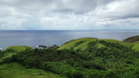 vista aérea cinematográfica de las impresionantes colinas cubiertas de selva frente a las aguas prístinas del océano y las nubes en la isla de catanduanes, filipinas