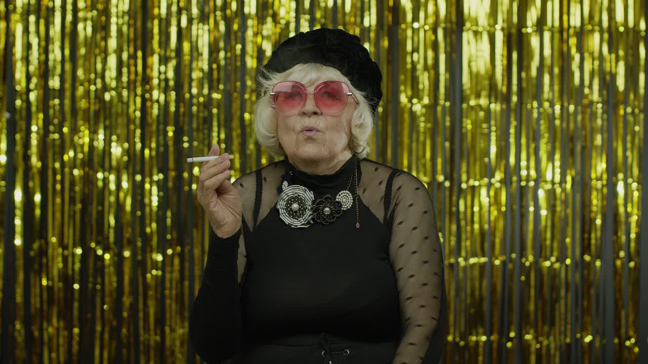 Ältere Dame in modischer schwarzer Kleidung mit Sonnenbrille posiert, raucht Zigarette.