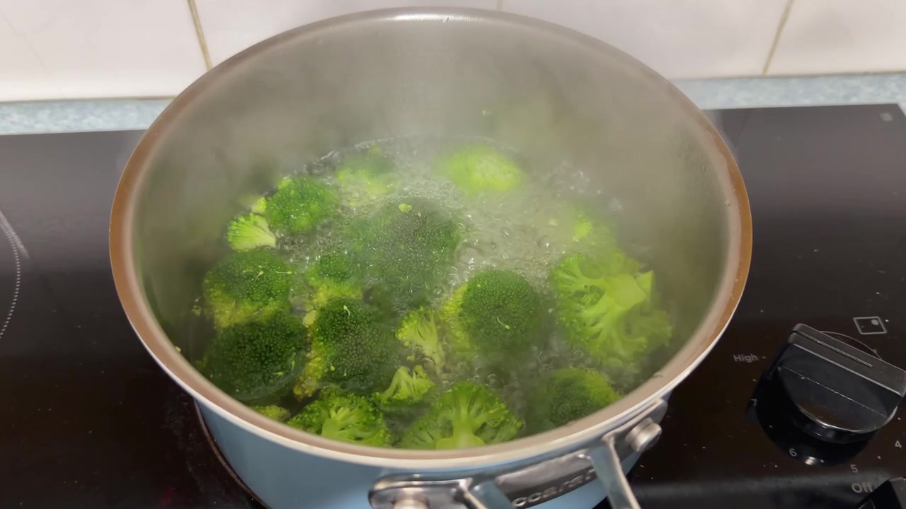 Cimette di broccoli verdi sobbollono in acqua bollente all'interno di una pentola fumante sul fornello