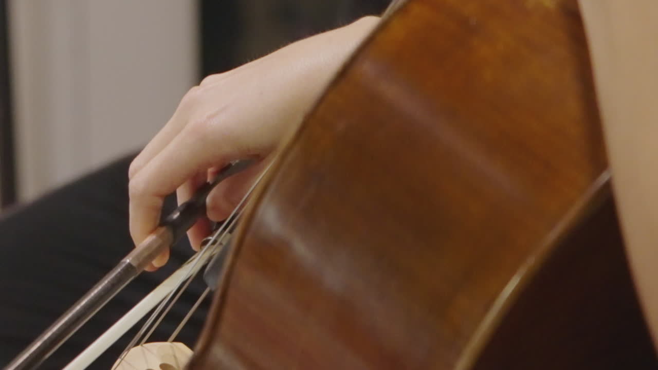 Primo piano di mano che suona il violoncello con l'archetto.