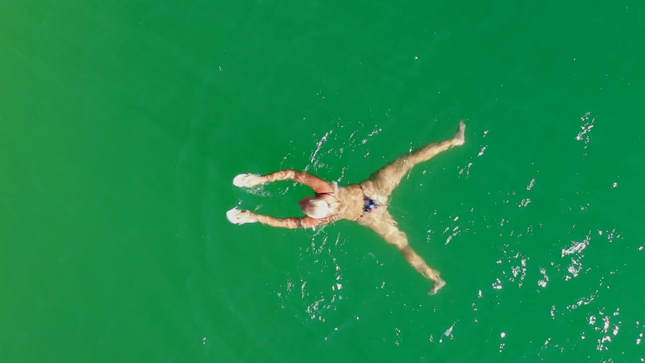 top down tracking of woman swimming in green lake, aerial view