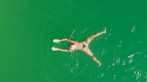 Seguimiento-De-Arriba-Hacia-Abajo-De-Una-Mujer-Nadando-En-Un-Lago-Verde,-Vista-Aérea