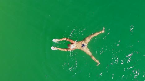 seguimiento de arriba hacia abajo de una mujer nadando en un lago verde, vista aérea