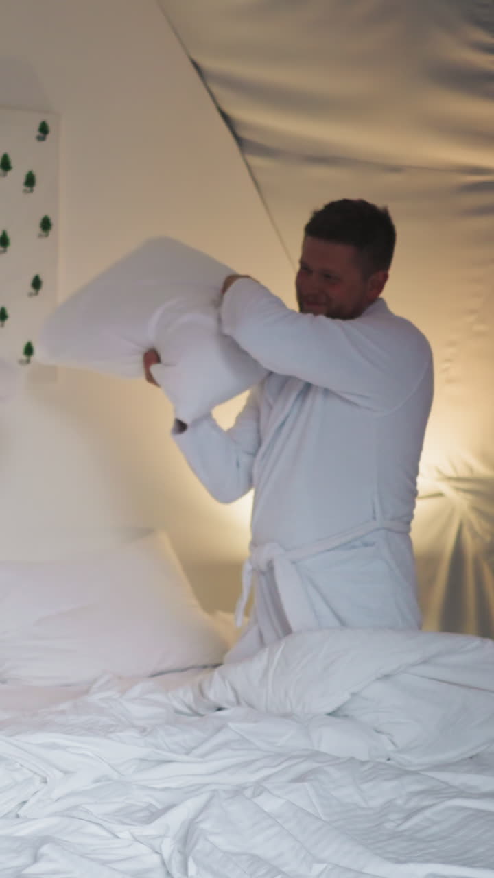 Couple plays pillow fighting on bed at glamping. Happy young man and woman enjoy playful fight in round tent house. Newlywed have fun on vacation