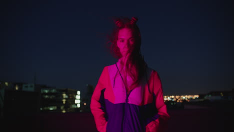 portrait teenage girl posing in city at night looking confident with urban style in red light wind blowing hair