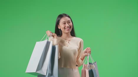 An Asian Shopping Woman With Shopping Bags Smile To Camera While Standing In Front Of Green Screen