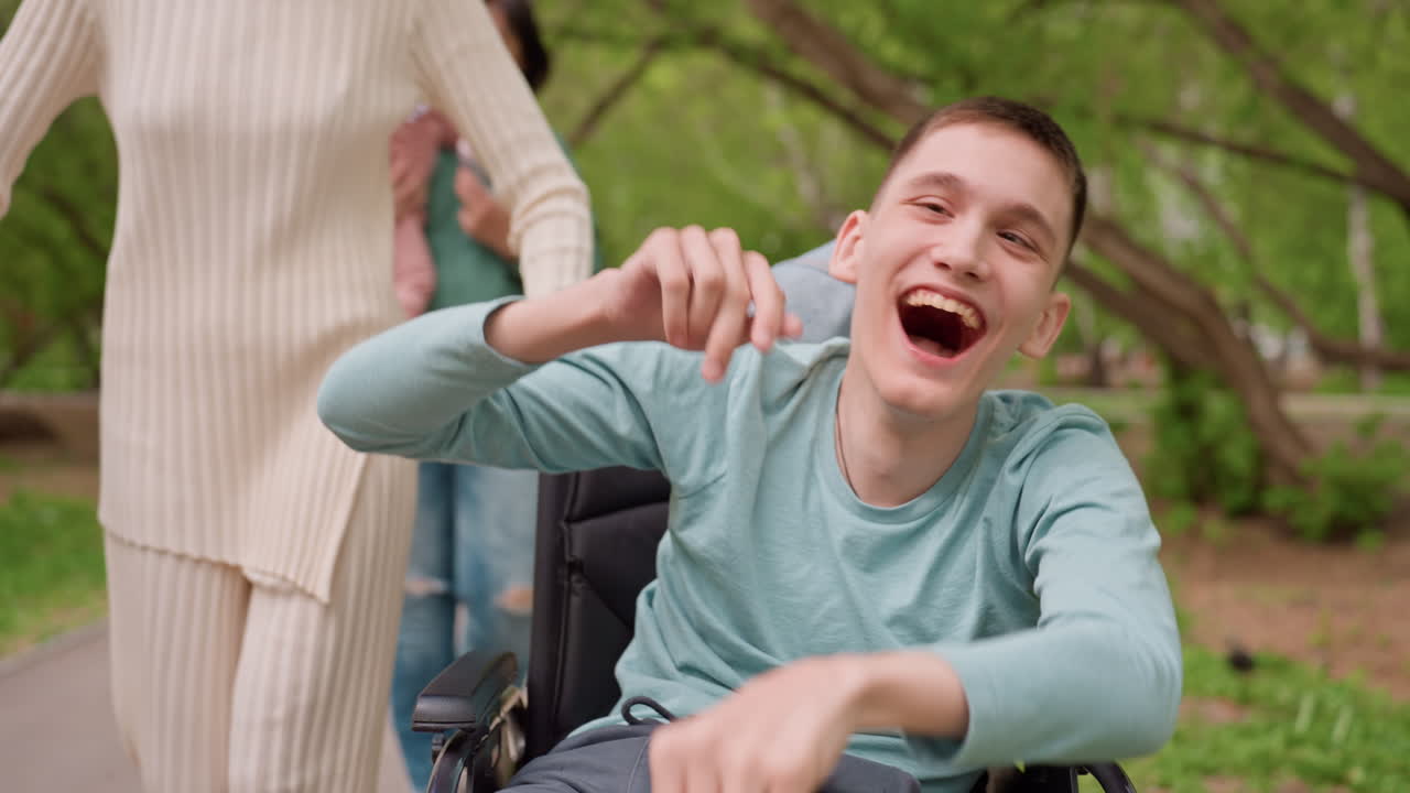 Young Man Laughing In Wheelchair Park Portrait, Caregiver Pushing From Behind, Bright Smile And Playful Pointing Gesture Captured In Natural Light Candid Emotional Moment Conveying Happiness