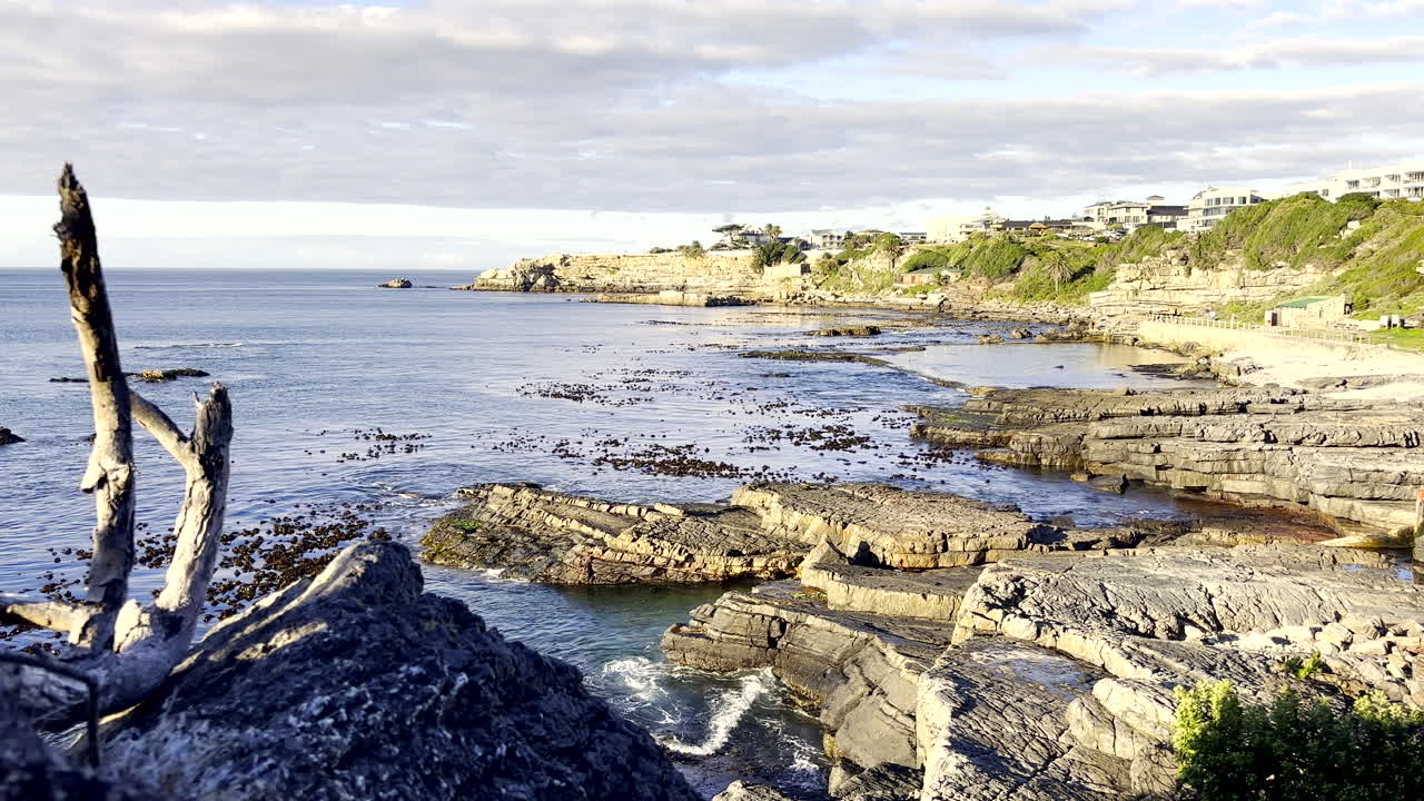Klippefyldt kystlinje ved Hermanus kystlandsby ved solopgang på en dag med stille hav.