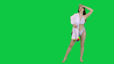 Model-in-a-bikini-and-a-towel-looking-of-a-spot-and-walking-away-in-front-of-a-green-screen