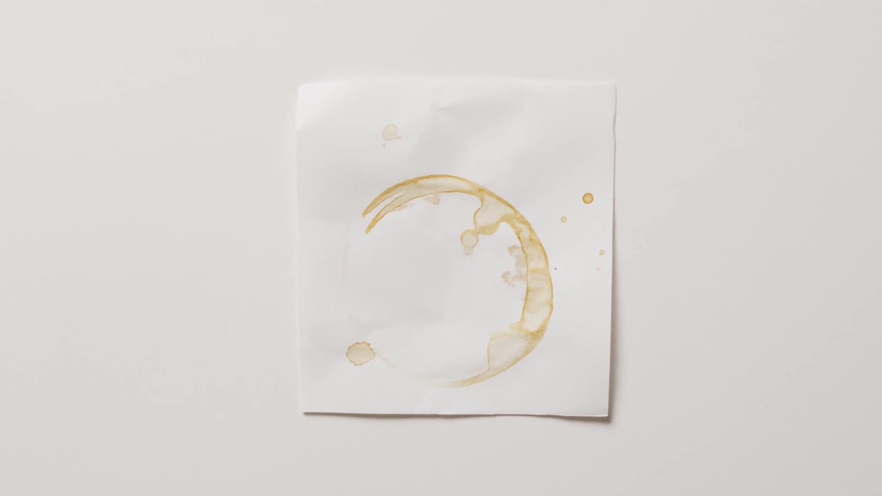 video de primer plano de un pedazo de papel con mancha de anillo de taza de café sobre un fondo blanco