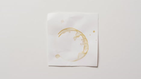 Video-of-close-up-of-piece-of-paper-with-coffee-mug-ring-stain-on-white-background