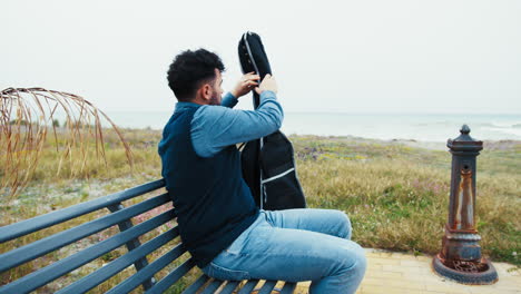 man opens the case to play his guitar near the sea