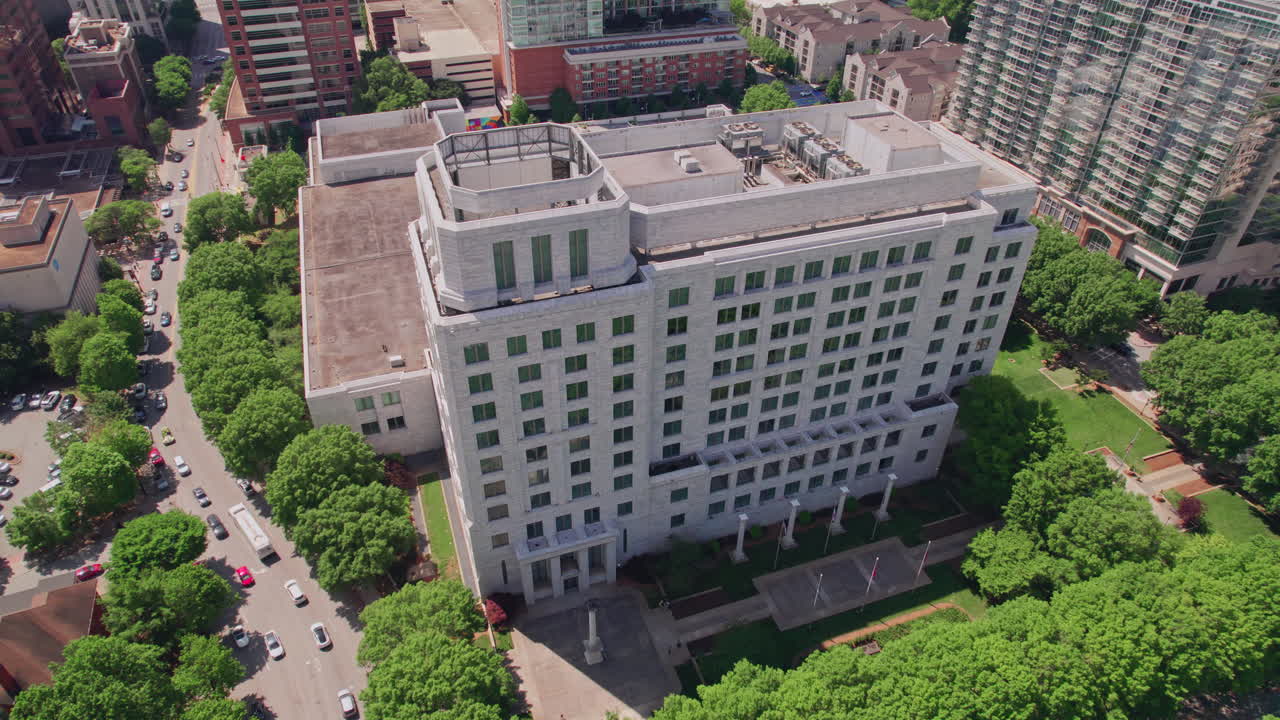 Vista aérea descendente do edifício de granito e mármore do Federal Reserve no centro de Atlanta, cercado por um exuberante dossel de árvores com o horizonte da cidade moderna ao fundo em um dia ensolarado de verão.