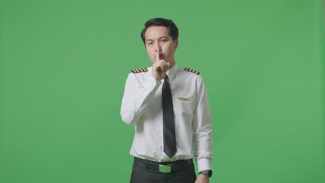 아시아 남성 조종사가 카메라를 바라보고 녹색 스크린 배경 스튜디오에서 shh 제스처를합니다.