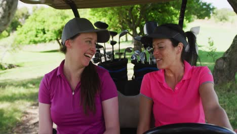 Two-caucasian-women-playing-golf-riding-a-golf-cart-talking-and-laughing
