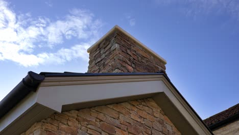 Small-luxury-stone-walled-cabin-building-with-wood-fired-chimney-poking-out-the-top-of-the-building-on-a-clear-blue-sunny-sky-day