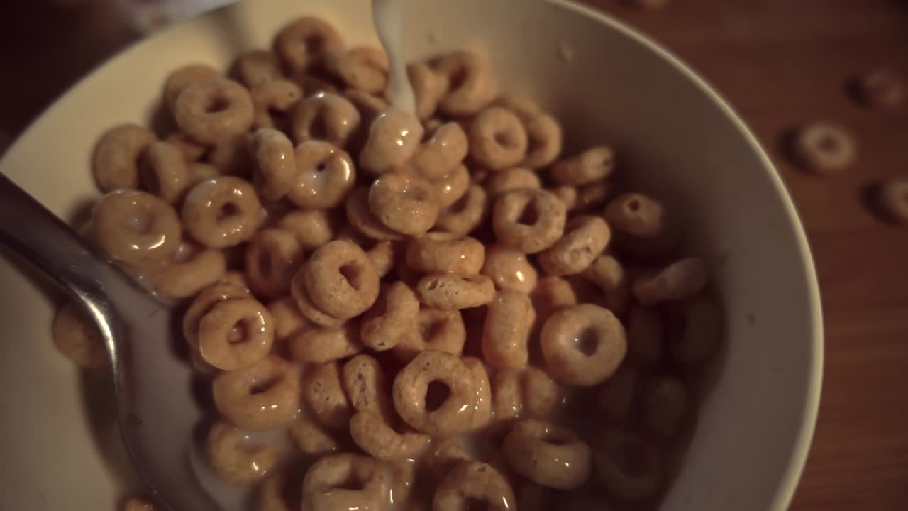 Close-up slow motion shot of milk being poured into a bowl of cereal in slow motion, highlighting texture and movement under warm indoor lighting