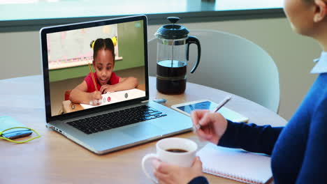 caucasian female teacher using laptop on video call with schoolgirl, making notes